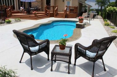 Swimming pool and patio with landscaping behind house with wooden deck